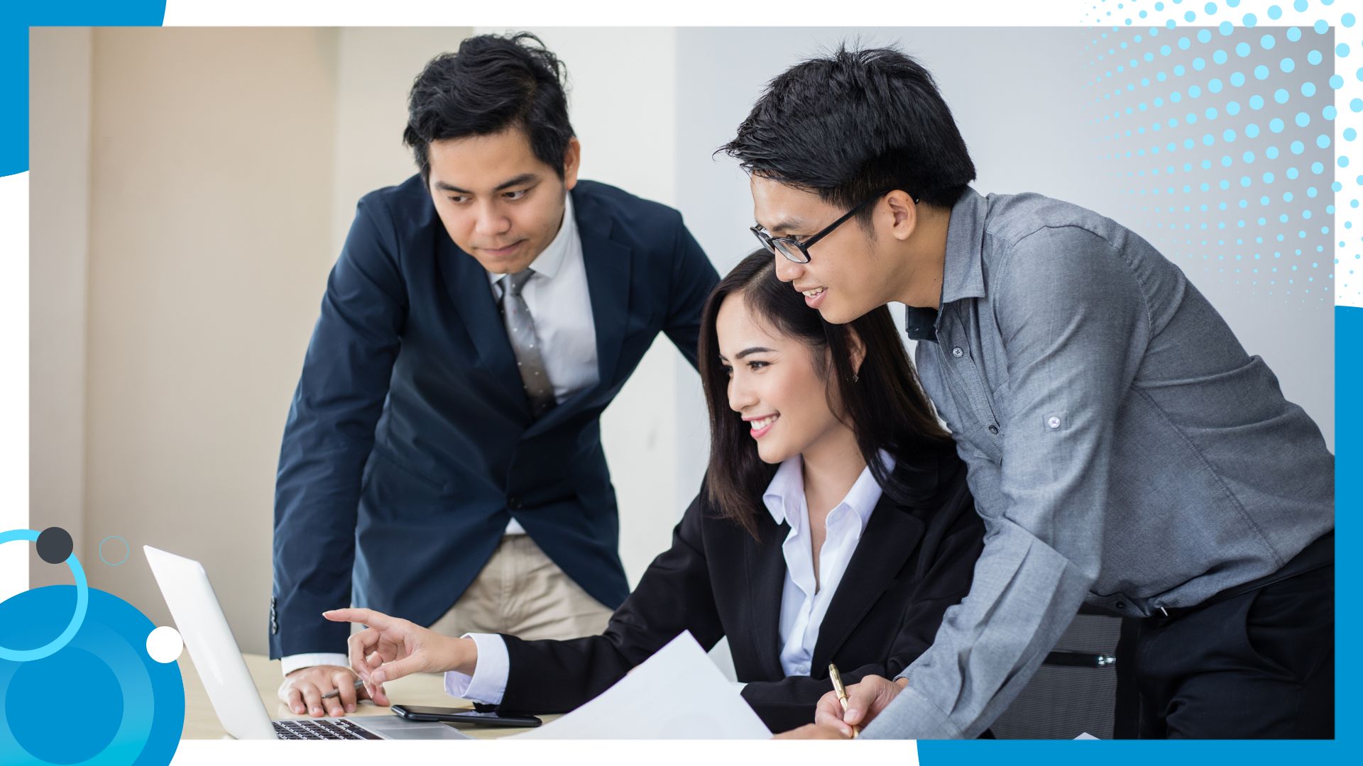 Three professionals collaborating in an office setting, reviewing content on a laptop and smiling, symbolizing teamwork and a productive work environment.